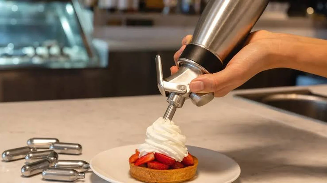 Whipped cream dispenser topping a strawberry dessert with fresh whipped cream
